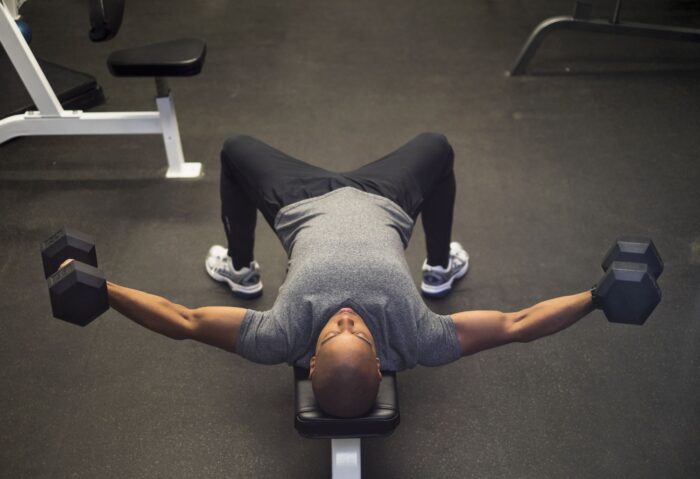 homem realizando o exercício crucifixo com halteres em um banco reto