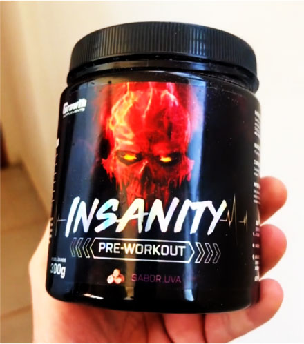 segurando um pote do pré-treino Insanity da Growth Supplements